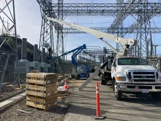 A boom truck and a lift working beneath the steel lattice structures of a high-voltage switchyard