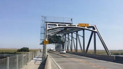 A steel through-truss bridge carrying a two-lane road across a delta channel