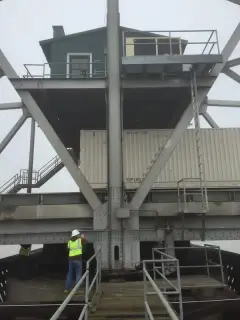 A green operator house raised on steel legs above a bridge deck, with a worker on the walkway below