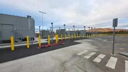 A finished standby power plant with equipment enclosures behind yellow bollards and a security fence