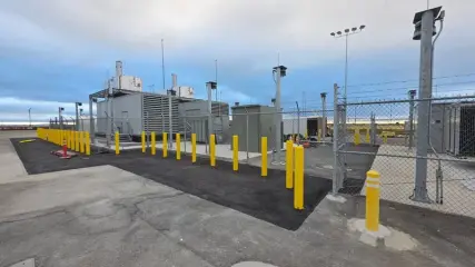 A completed standby power installation on a paved pad, enclosed by a chain link fence with hills behind