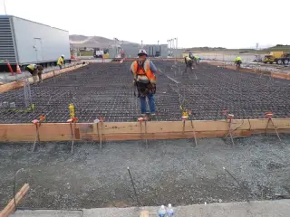 A worker standing on a large tied reinforcing steel mat inside timber formwork