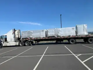 A flatbed trailer loaded with metal-clad electrical equipment parked on an open apron