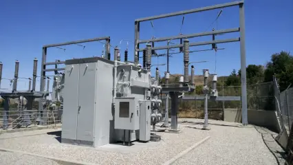 A completed substation bank with a transformer, steel structures and bushings behind a wall