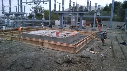 A large rectangular concrete foundation with timber edge forms in a fenced substation compound