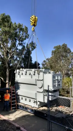 A large power transformer on a low trailer being manoeuvred along a narrow tree-lined access road