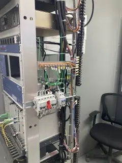 An equipment rack with relays, terminal strips and fiber patch cords, an office chair beside it