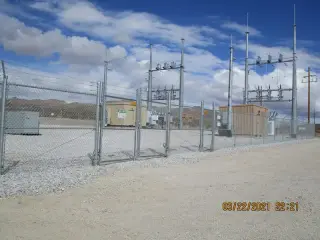 A finished substation seen through its perimeter fence, with equipment enclosures and gravel surfacing