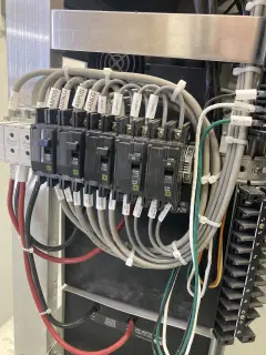 A row of small breakers with labelled grey control cables looping into them and red and black battery leads below