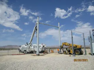 A line truck and a telehandler positioned beside tall steel structures in an open desert substation