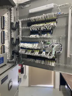 An open control cabinet door carrying rows of terminal blocks with neatly dressed, labelled white wiring