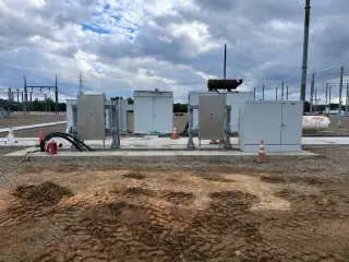 Several grey metal-clad electrical cabinets standing on a new concrete pad in a substation yard under a cloudy sky