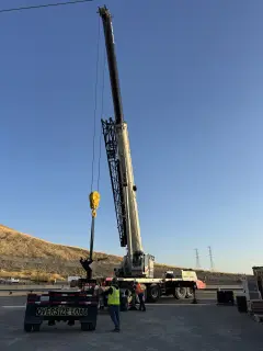A crane boom extended overhead above a trailer carrying an oversize load placard