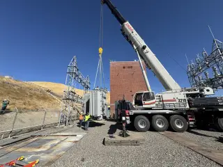 A wide view of a pumping plant with a mobile crane rigged beside the switchyard and a crew working at the base