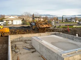 A finished concrete equipment foundation with a wheeled loader working on backfill alongside