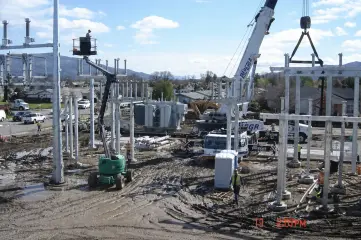A crane setting galvanised steel structures at a muddy substation site with hills behind