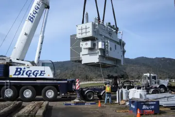 Two mobile cranes lifting a large power transformer clear of a low trailer