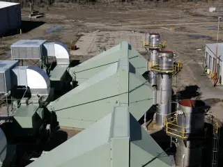 Roof-level view across green turbine enclosures and stainless exhaust stacks with access platforms