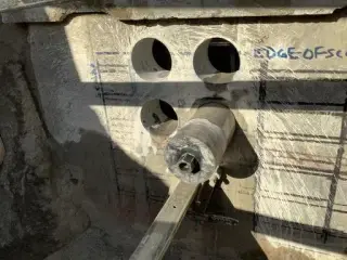 A core drill bit against a concrete wall with three round cored holes and scanned rebar lines marked in ink