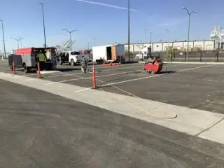 Work trucks, a trailer and a concrete saw on a paved lot marked out with orange delineators