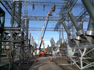 A substation bay seen past insulator stacks and steel structures, with a crane boom standing behind