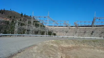 A switchyard on a hillside seen from an access road, with rows of steel structures against the sky