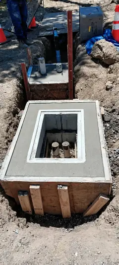 A concrete pull box with a metal frame and lid being set into an excavation