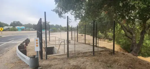 A completed pumping plant site enclosed by new chain link fence beside a highway guardrail