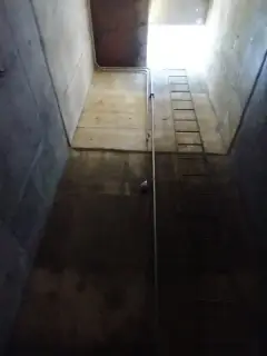The interior of a deep rectangular concrete wet well with a fixed access ladder running down one wall