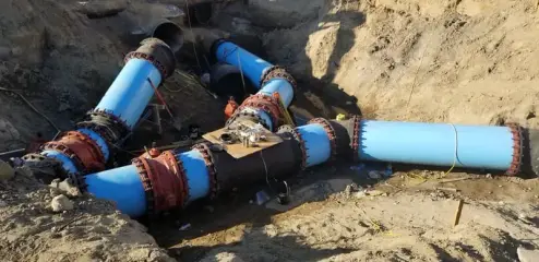 Large blue ductile iron pipes and fittings joined together in an open excavation