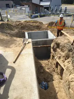 A rectangular precast concrete vault sitting in an open excavation with spoil piled alongside