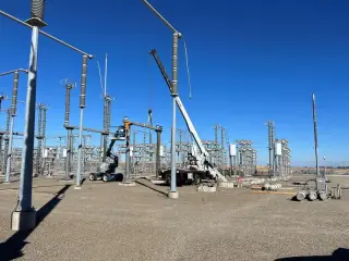 A crane boom and rigging lifting a long insulator string in a high-voltage substation yard