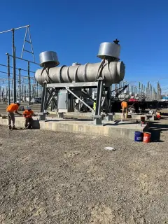 A cylindrical reactor unit slung in red rigging straps and lowered onto a galvanised steel stand
