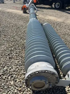 A long cylindrical shunt reactor with fins lying on gravel, waiting to be lifted into place
