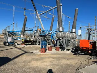 Substation bay under construction with a crane, a boom lift and crews working beneath large 500kV bus insulators
